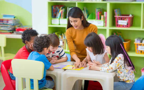 アジア女教師教室、幼稚園前の学校のコンセプトで本を読んで混血の子供たちを教えます。 - 幼稚園教師 ストックフォトと画像