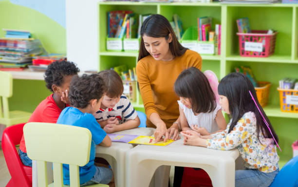Asian female teacher teaching mixed race kids reading book in classroom,Kindergarten pre school concept. Asian female teacher teaching mixed race kids reading book in classroom,Kindergarten pre school concept asian kids learning stock pictures, royalty-free photos & images
