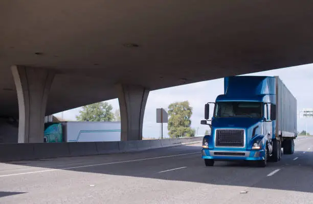 Photo of Big rig blue semi truck going under bridge