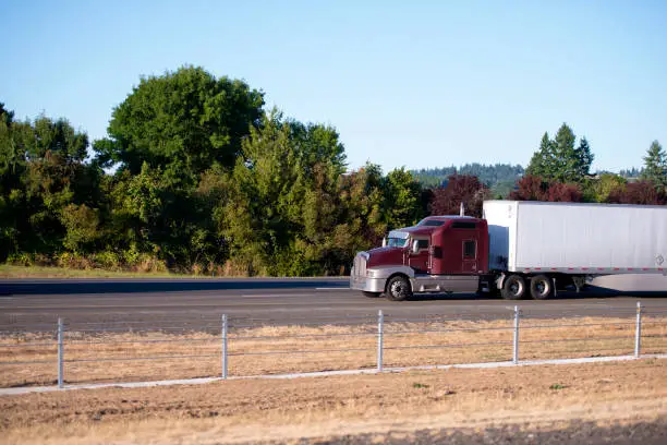 Photo of Big rig powerful semi truck with dry van trailer move ahead on straight highway road with divided traffic lines