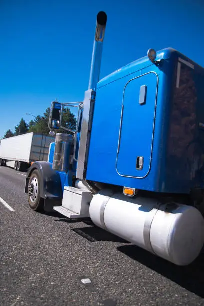 Photo of Blue big rig semi truck with high tailpipes and an extended drivers cab is moved along the road with traffic