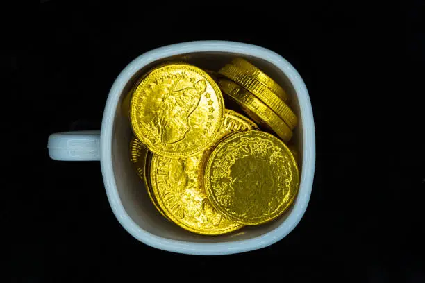 top view of a a white cup full of gold coins on dark backbround