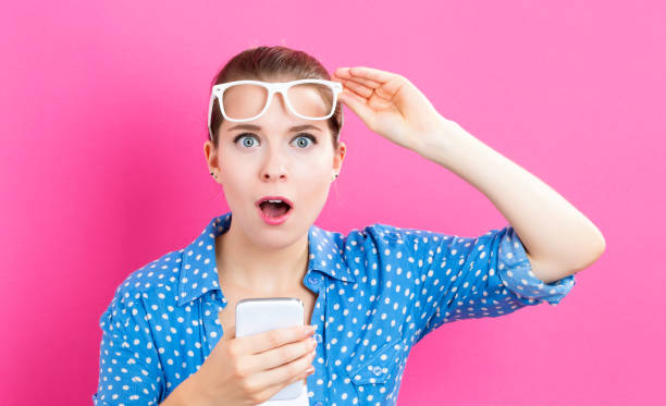 Young woman using her phone Young woman using her phone on a pink background solid colour stock pictures, royalty-free photos & images