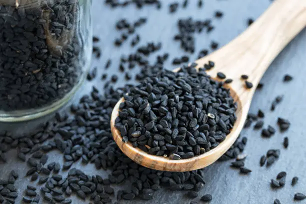 Black cumin seeds on a wooden spoon on gray background