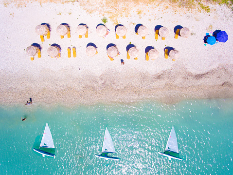 Summer beach in Lefkada Greece with sun umbrellas and sunbeds and yachts in the water