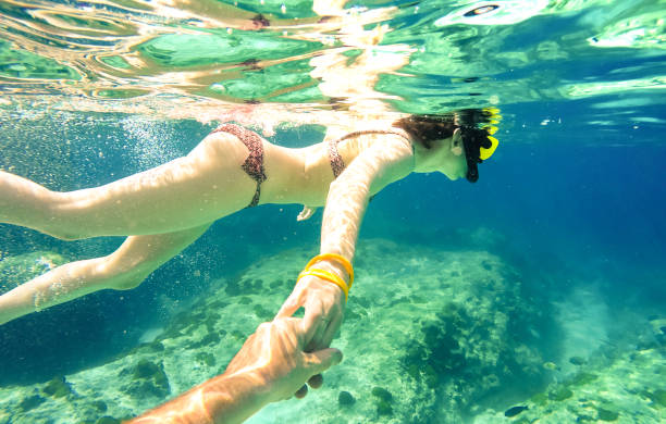 snorkel couple swimming together in tropical sea with follow me composition - snorkeling tour in exotic diving scenarios - fun travel concept with active girl underwater - soft focus due water density - vacations couple travel destinations snorkeling imagens e fotografias de stock
