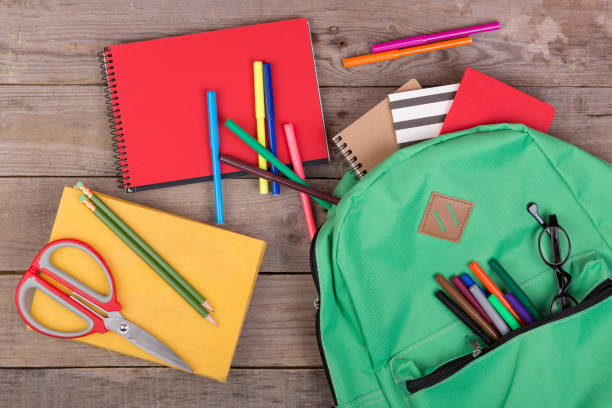istock Backpack and school supplies: books, pencils, notepad, felt-tip pens, eyeglasses, scissors on brown wooden table 870445780