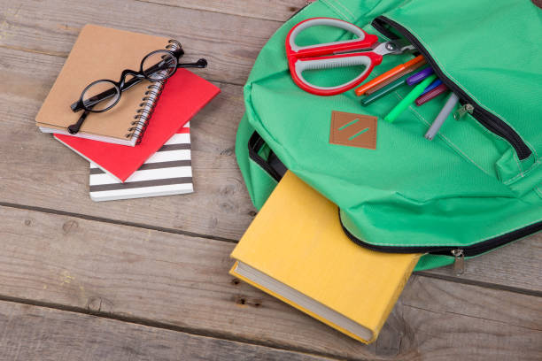 istock Backpack and school supplies: books, pencils, notepad, felt-tip pens, eyeglasses, scissors on brown wooden table 870445808