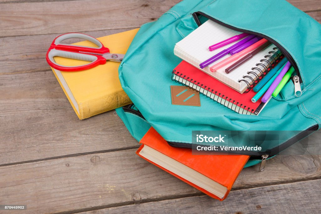 Backpack and school supplies: books, notepad, felt-tip pens, scissors on brown wooden table School Supplies Stock Photo