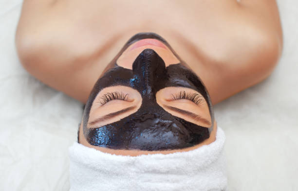 el procedimiento para la aplicación de una máscara negra en la cara de una mujer hermosa. - mud wellbeing spa treatment beautician fotografías e imágenes de stock
