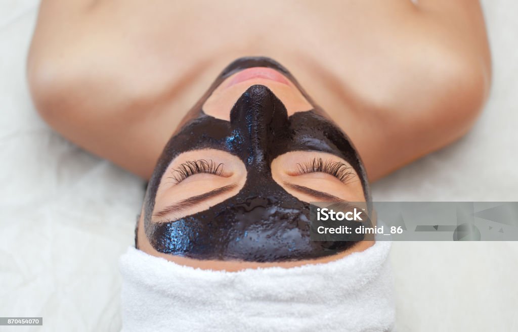 The procedure for applying a black mask to the face of a beautiful woman. The procedure for applying a black mask to the face of a beautiful woman. Spa treatments and care of the cats in the beauty salon. Coal Stock Photo