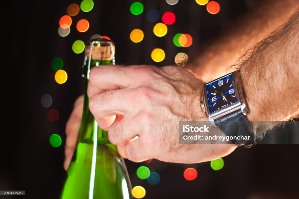 Opening a bottle of sparkling wine like champagne, a man's hand with a watch, New Year's lights, happy new year and Christmas, celebration 2018 Adult Stock Photo