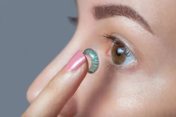 Photo of woman holds a blue contact lens on her finger.