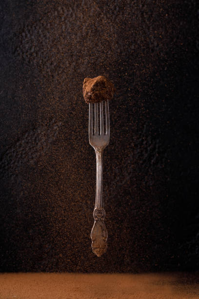 Candy truffle on a dessert fork levitating on a black background. Candy on a beautiful antique fork with a pattern. Homemade truffle on a black background, on which cocoa is poured on top. stock photo