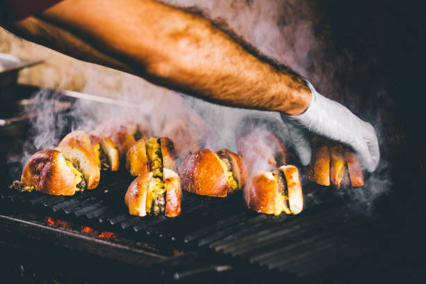 Hand cooking burgers on a hot flaming grill Detail of chef hands with gloves cooking cheeseburgers on a hot flaming grill smoke and flames bbq for an outdoor festival food festival stock pictures, royalty-free photos & images