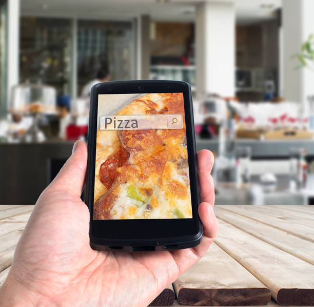 istock Hand holding smart phone with pizza search against indoor restaurant background 870481484