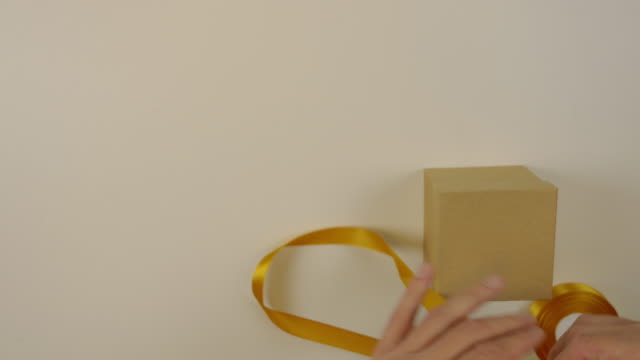 Preparation for gift wrapping. A box of brown cardboard. Mens hands measure the gold satin ribbon to decorate the gift box. Top view close up.