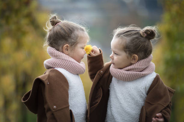 Two identical twin girls smelling a flower