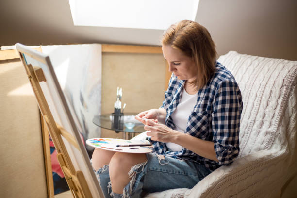 istock Happy young woman paints on canvas 870492284