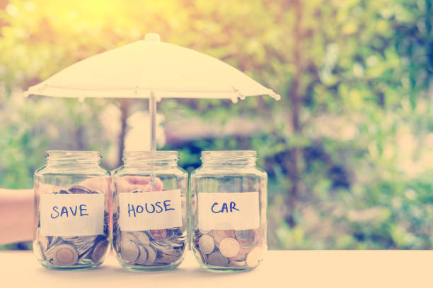 Saving money for house and car concept : Coins in jars under an umbrella. Ideas of saving for a down payment on a car or home that allow buyers to use down payment to reduce overall cost of borrowing Saving money for house and car concept : Coins in jars under an umbrella. Ideas of saving for a down payment on a car or home that allow buyers to use down payment to reduce overall cost of borrowing deposit bottle stock pictures, royalty-free photos & images