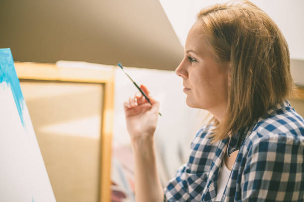 istock Happy young woman paints on canvas 870517478