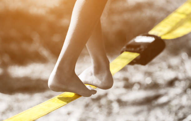 Tightrope walker is on a tight sling which is fixed on the trees at a low altitude. Tightrope walker is on a tight sling which is fixed on the trees at a low altitude. Slasklining extreme sport a balancing act. safety net stock pictures, royalty-free photos & images