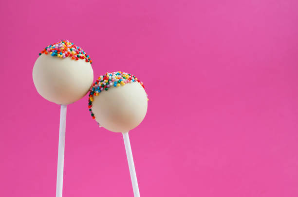 istock White chocolate cake pops decorated with colorfull confectionery sprinkles on a pink background. Concept sweet couple. 870536234