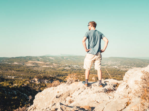 istock Young Man Standing on top of a Cliff, looking across a valley 870539016
