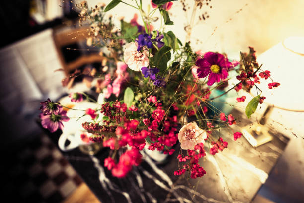 Plastic flowers glass vase on wooden table in blurred bakery shop with selective focus