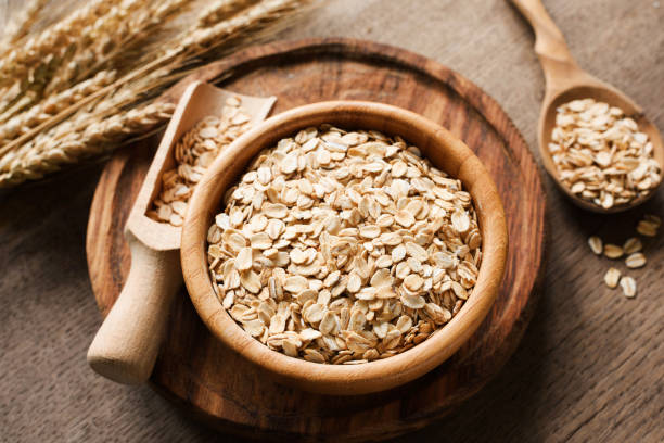 Rolled oats, organic oat flakes in wooden bowl and golden wheat ears on wooden background stock photo