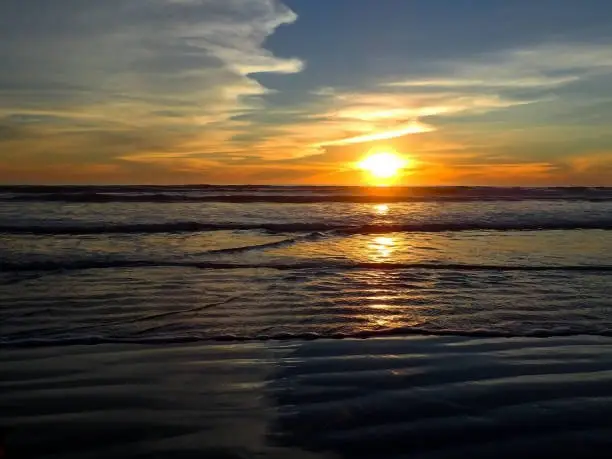 This is a sunset image with zig zag patterns mimicked in the sand, the waves, and the clouds in the sky.