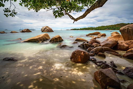 Sailboats, catamarans and granite rocks in the indian ocean on a cloudy day at world famous beach anse lazio, praslin, seychelles