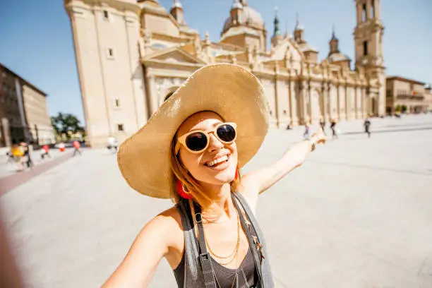 Young woman tourist making selfie photo in front of the famous cathedral on the central square during the sunny weather in Zaragoza city, Spain