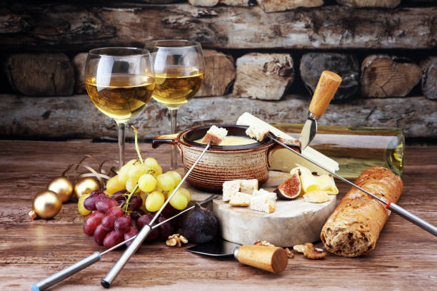 istock Gourmet Swiss fondue dinner on a winter evening with assorted cheeses on a board alongside a heated pot of cheese fondue with two forks dipping bread and white wine behind in a tavern or restaurant. 870588090