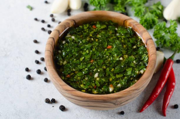 Traditional argentinian chimichurri sauce made of parsley, cilantro, garlic and chili pepper in a wooden bowl. Selective focus, horizontal image A wooden bowl wirh homemade fresh chimichurri sauce standing on a wooden board with ingredients chimichurri stock pictures, royalty-free photos & images