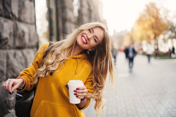 mujer joven feliz con estilo usando boyfrend jeans, zapatillas blancas sweetshot de amarillo brillante. tiene café para llevar. retrato de niña sonriente en gafas de sol y con la bolsa de - women spring sensuality fashion model fotografías e imágenes de stock