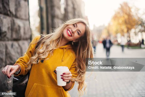 Photo libre de droit de Élégante Heureuse Jeune Femme Porte Un Jeans Boyfrend Baskets Blanc Lumineux Jaune Sweetshot Elle Est Titulaire De Café Pour Aller Portrait De Jeune Fille Souriante Dans Lunettes De Soleil Et Avec Sac banque d'images et plus d'images libres de droit de Femmes