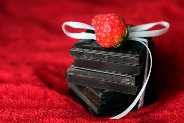 Dark chocolate squares with a strawberry on a red cloth.