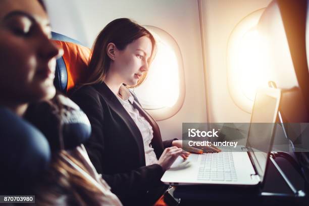 Female Entrepreneur Working On Laptop Sitting Near Window In An Airplane Stock Photo - Download Image Now