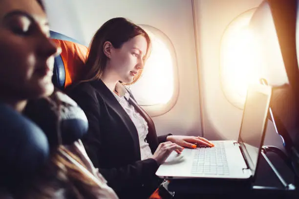 Female entrepreneur working on laptop sitting near window in an airplane.