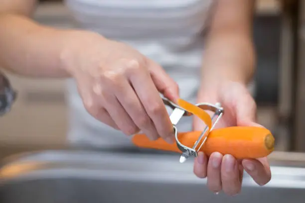 closeup of housewife's hands peeling carrot in the kitchen, photographed naturally without heavy processing