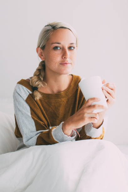 istock Serious young woman sitting on bed holding cup 870722326