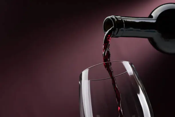 Pouring red wine from a bottle into a wineglass: wine tasting and celebration