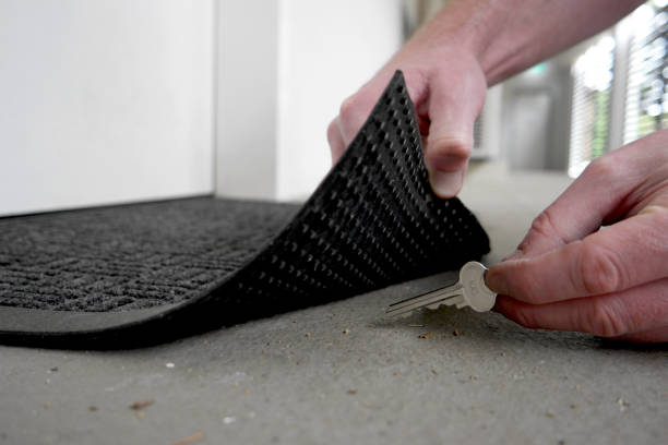 Man lifting edge of a door mat to pick up a key hidden underneath A man's hand is picking up or returning key under the door mat key doormat stock pictures, royalty-free photos & images