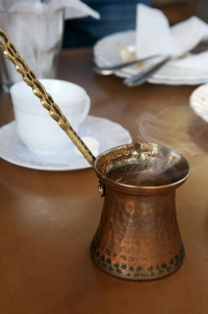 Fresh hot coffee in copper cezve on brown table.