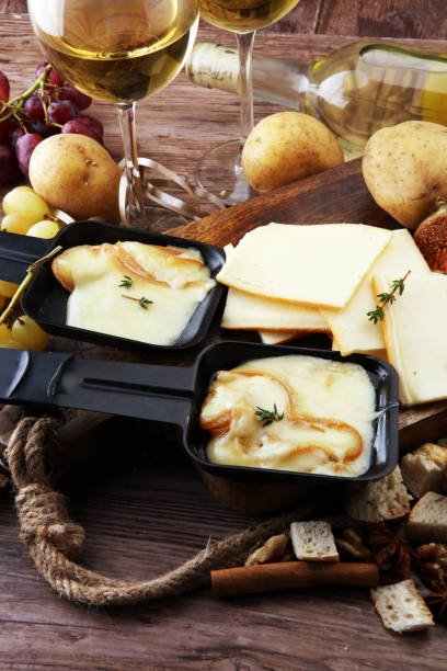 вкусный традиционный швейцарский плавленый сыр раклетт на нарезанный кубиками отварной или запеченный картофель подается в индивидуальн� - raclette cheese стоковые фото и изображения
