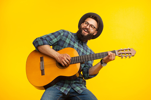 Smiling bearded musician man having fun and playing acoustic guitar.
