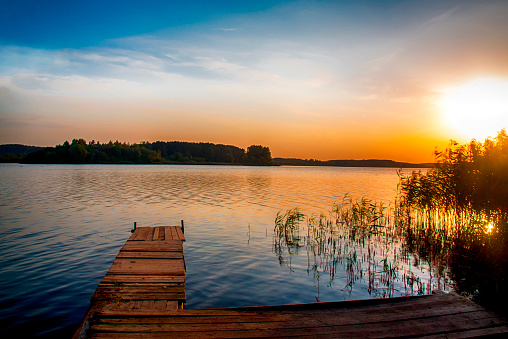 Perspective view of a wooden pier on the pond at sunset.