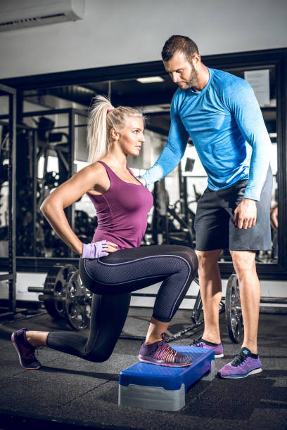 Lunge exercise with personal trainer Young attractive blonde female doing lunge exercise in modern fitness center with assistance of her personal trainer. blonde female bodybuilders stock pictures, royalty-free photos & images