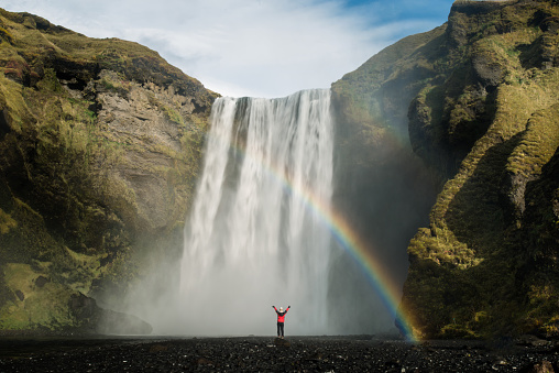 Beautiful nature, Skogafoss waterfall with rainbow in front and tourists are raising arms, Iceland